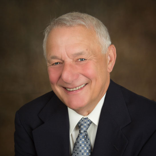 Jerald Eichelberger - Smiling business professional in a checkered blazer having a conversation across a table in a modern office lounge, with other professionals engaging in background discussions.