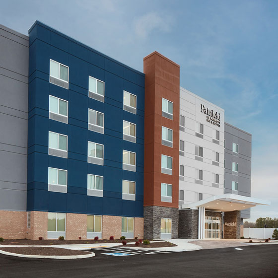 Modern exterior of Fairfield Inn & Suites by Marriott in Stony Creek, featuring a colorful multi-tone facade with blue, red, and gray sections, large windows, and a covered entrance against a clear sky.